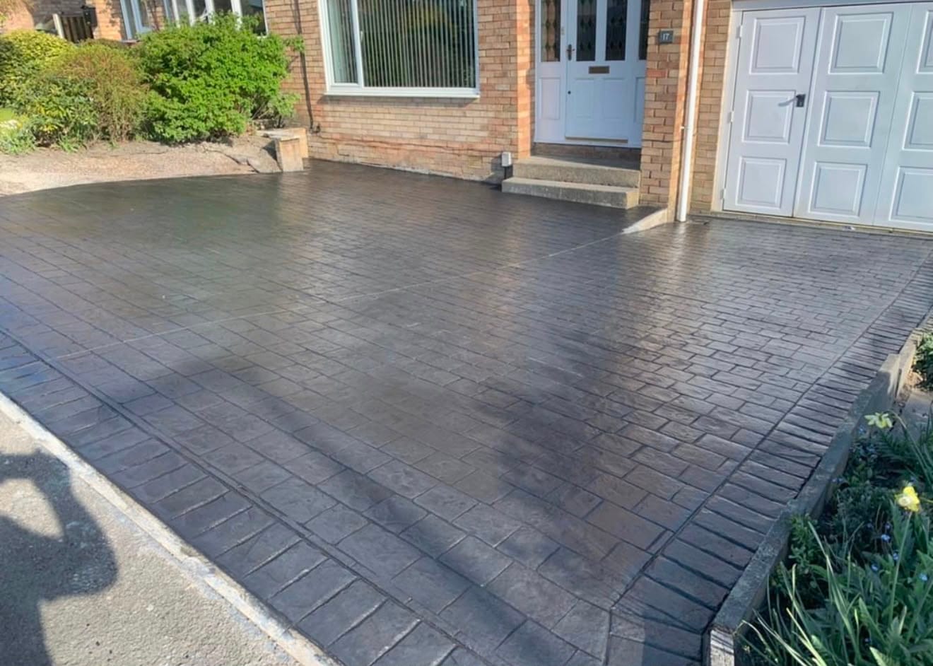 Brindle brown brick-pattern imprinted concrete driveway laid from the kerb up to a garage and front door in the sun