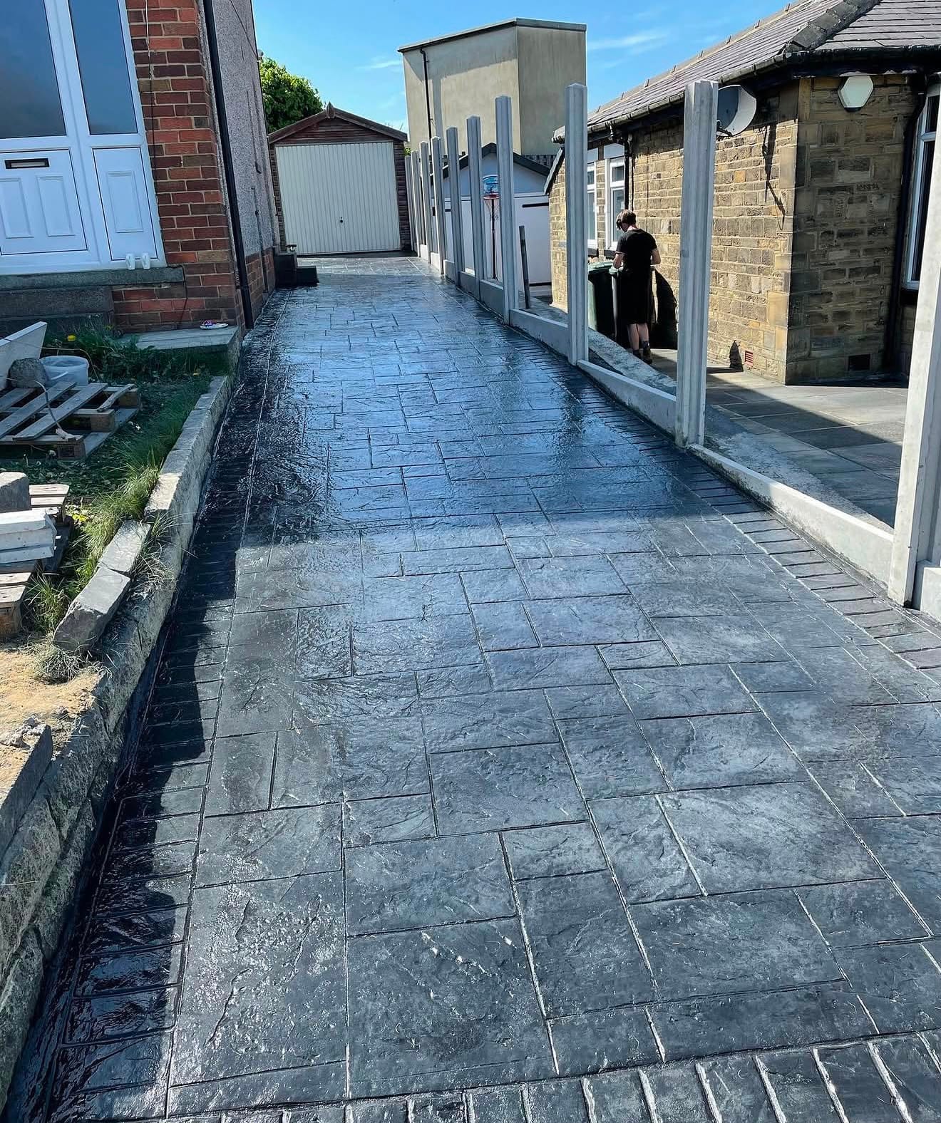 Charcoal ashlar pattern imprinted concrete side path running between two houses, freshly wet-sealed in the sun