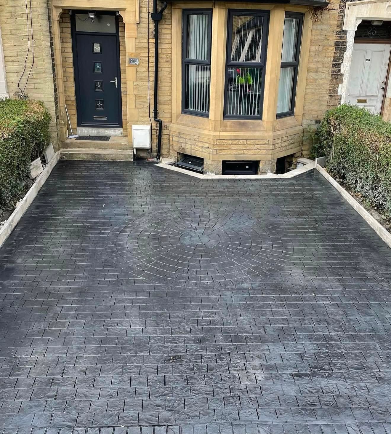 Charcoal ashlar imprinted concrete driveway with a central circle feature in front of a period stone bay-window house