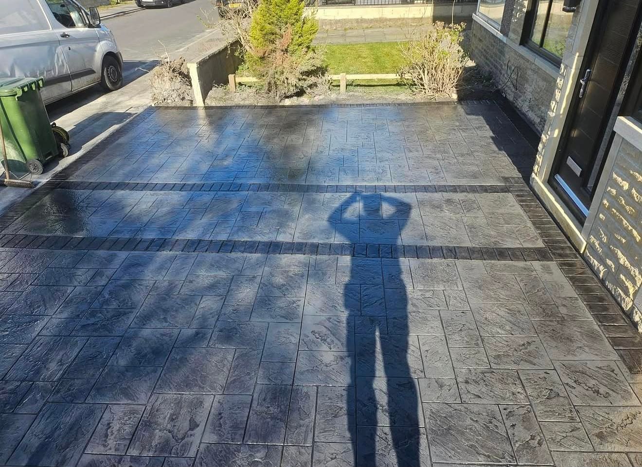 Large charcoal riven-slab imprinted concrete driveway framed by a double contrasting banded border in the sun