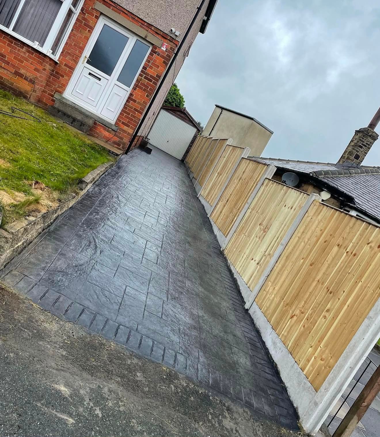 Charcoal imprinted concrete driveway sloping down to the road beside newly installed timber fencing
