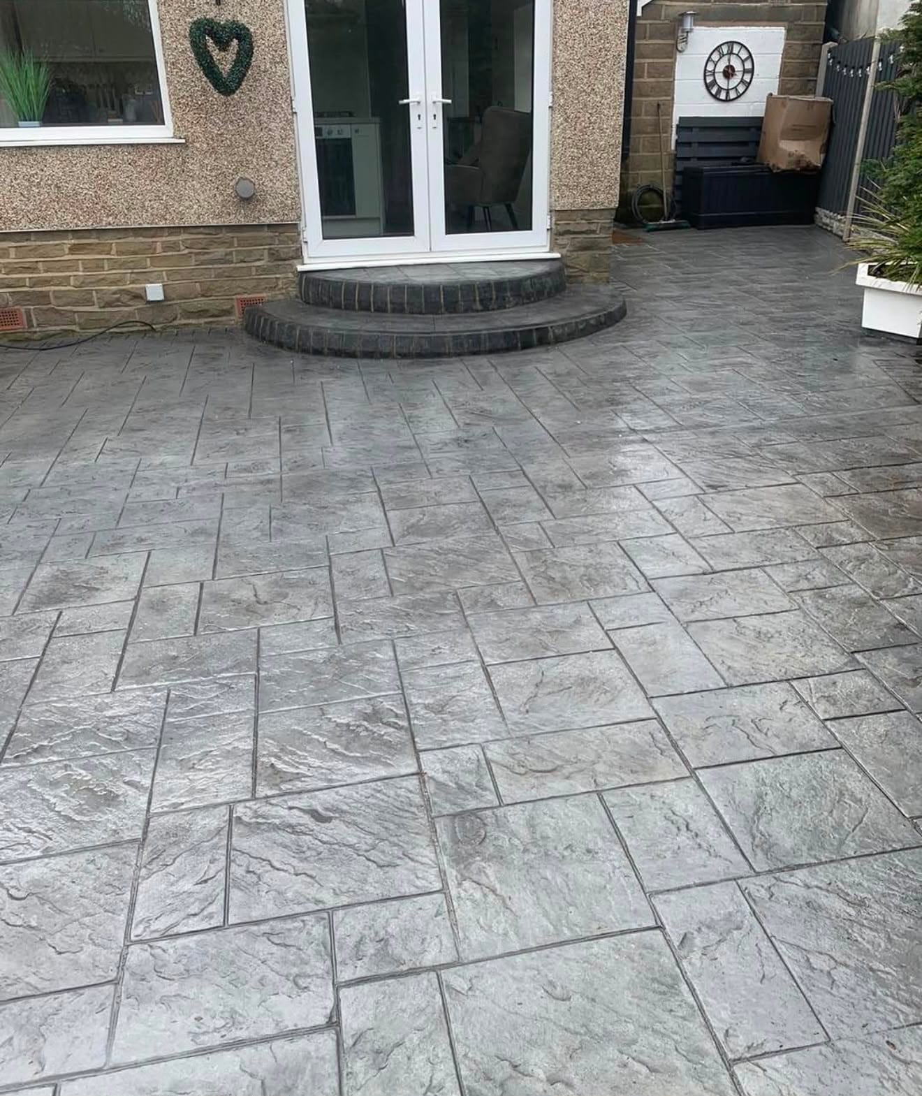 Grey riven-slab imprinted concrete patio with a stepped threshold leading to white French doors