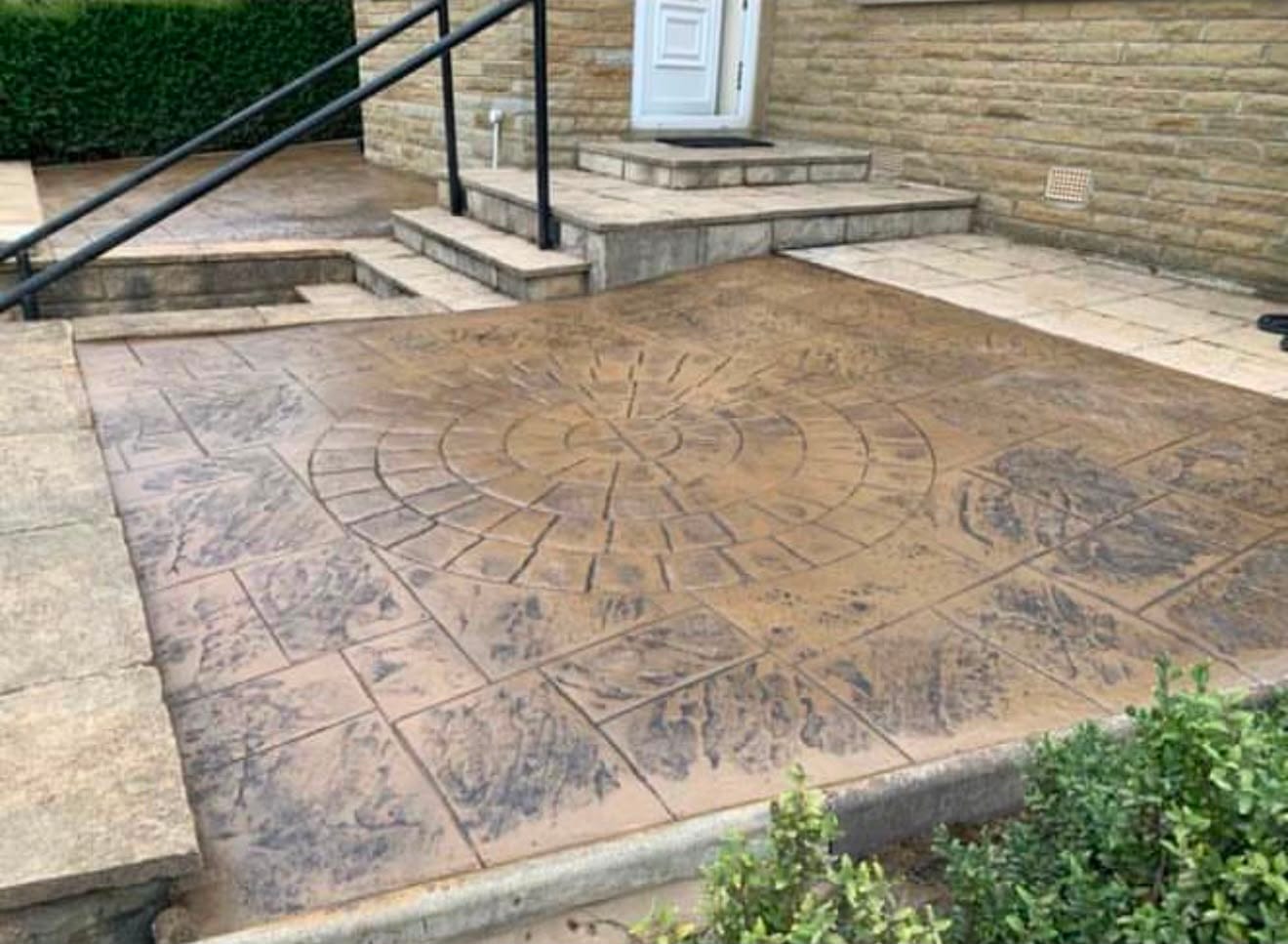 Sandstone imprinted concrete patio with a detailed compass circle feature and matching steps up to a stone house