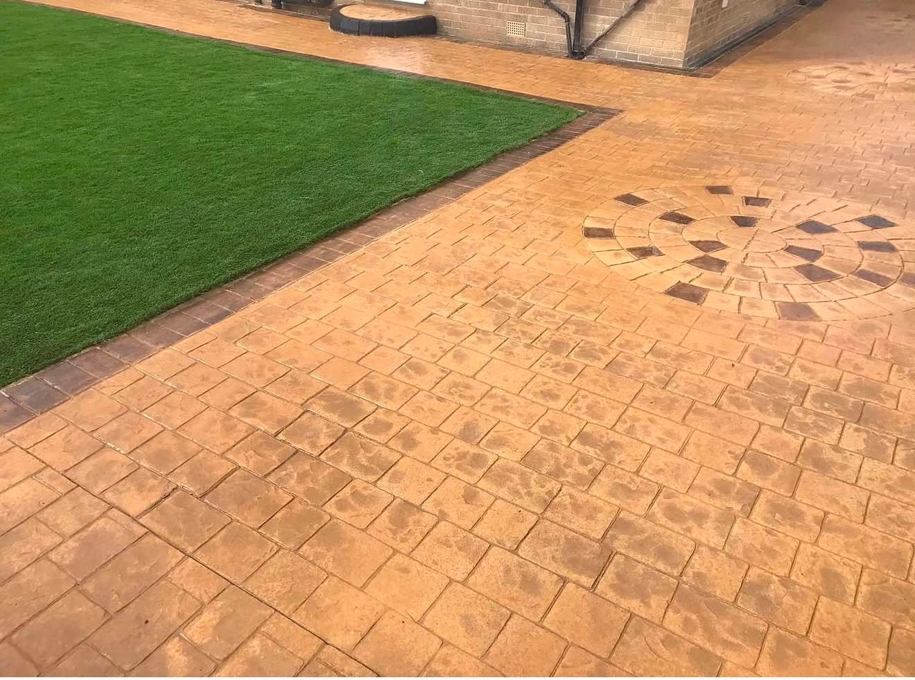 Buff sandstone imprinted concrete patio with a dark sunburst circle feature laid beside a run of artificial lawn