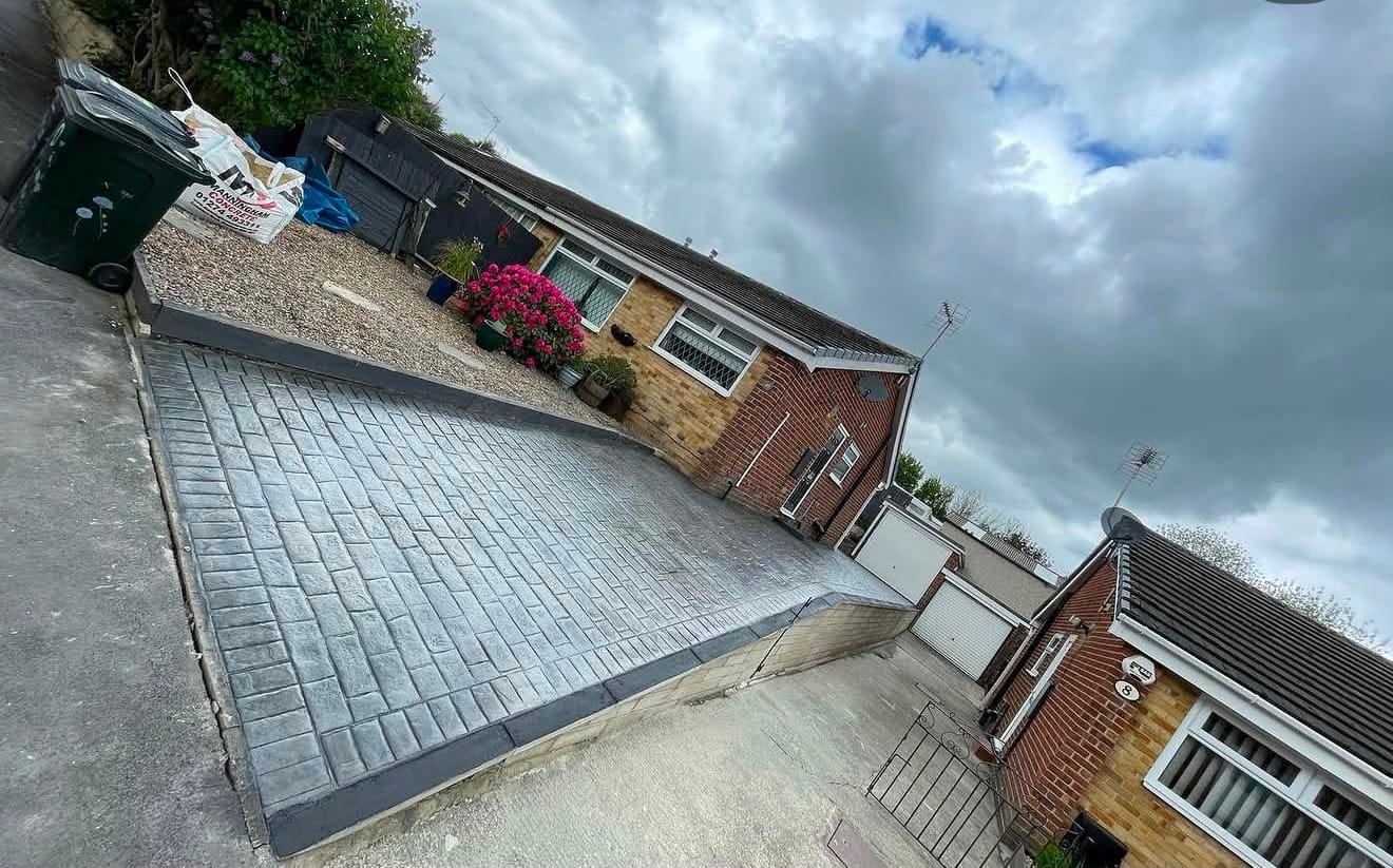 Slate imprinted concrete driveway laid to a brick bungalow with a darker charcoal border, flowers in bloom alongside